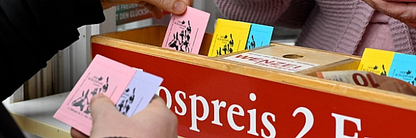 Hand zieht Lose aus dem Holzkasten der Bürgerparktombola.