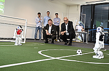 Bürgermeister Andreas Bovenschulte schaut einem Roboter des DFKI beim Fußball spielen zu.