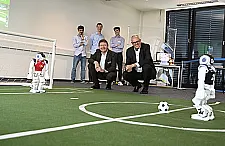 Bürgermeister Andreas Bovenschulte schaut einem Roboter des DFKI beim Fußball spielen zu.
