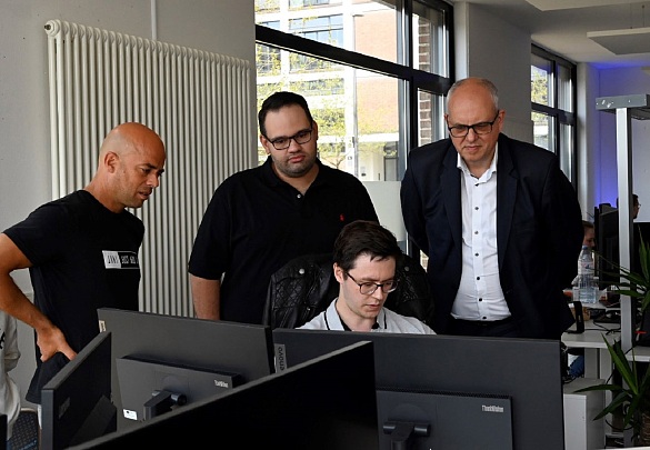 Die Geschäftsführer von JUSTADD AI, Roland Becker (links) und Julian Moeser (Mitte) sowie ihr Mitarbeiter Aljoscha Niazi-Shahabi (sitzend) erläutern Bürgermeister Andreas Bovenschulte die Entwicklung von KI-basierten Programmen.